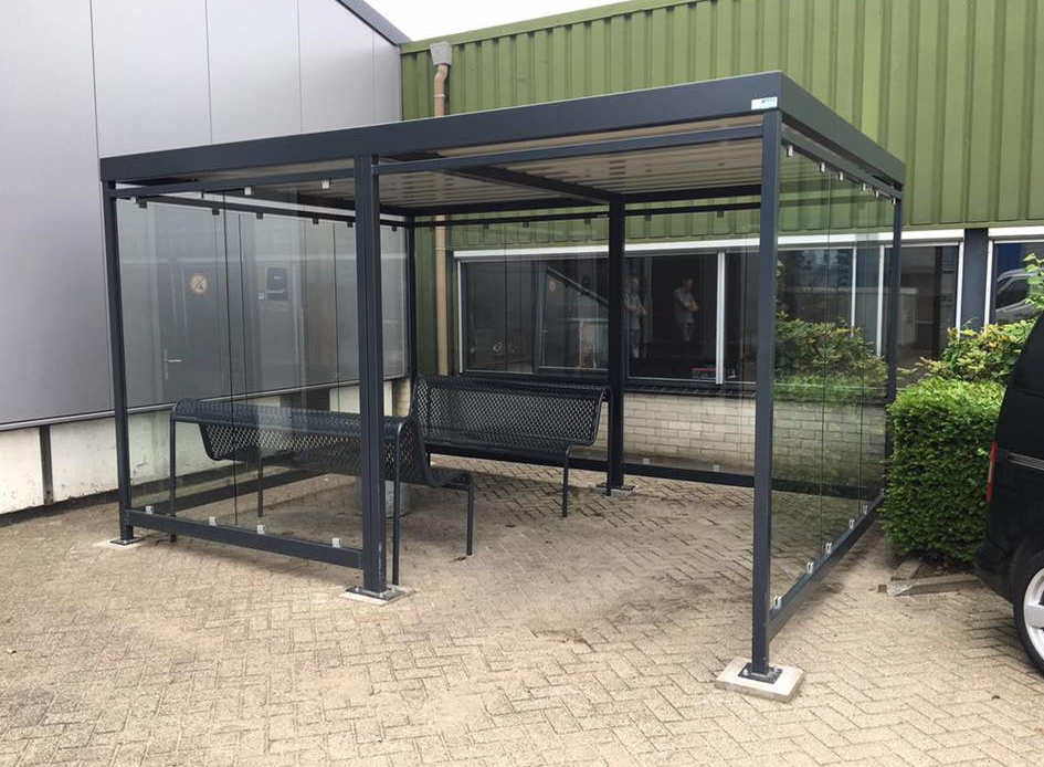 Wat kost een rookoverkapping? Prijzen en mogelijkheden in 2026 7 Rookoverkapping in de afmetingen 4 x 3 meter, voorzien van 2 van onze parkbanken model Station. Zowel de rookoverkapping als de banken gepoedercoat in antraciet-grijs